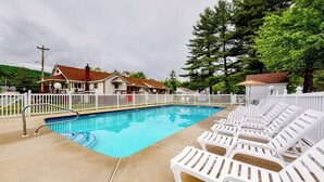 Una piscina con sillones de descanso, una valla blanca y casas al fondo.