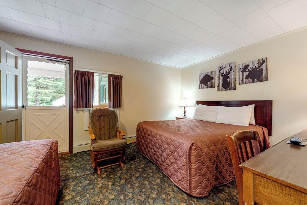 Een hotelkamer met een bed, een stoel, een bureau, een raam met gordijnen en wanddecoratie.