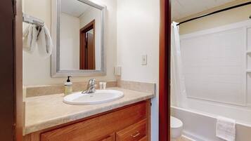 A bathroom with a sink, mirror, wooden vanity, and a white bathtub.