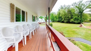 A covered porch with white plastic chairs, a wooden deck, and a view of a green lawn and trees. - Charming and causal motel in a great location with shared resort amenities (Lincoln)