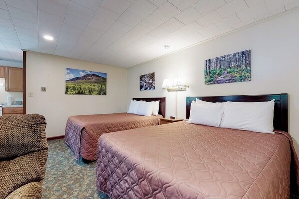 A hotel room with two beds, a chair, a desk, and artwork on the walls.