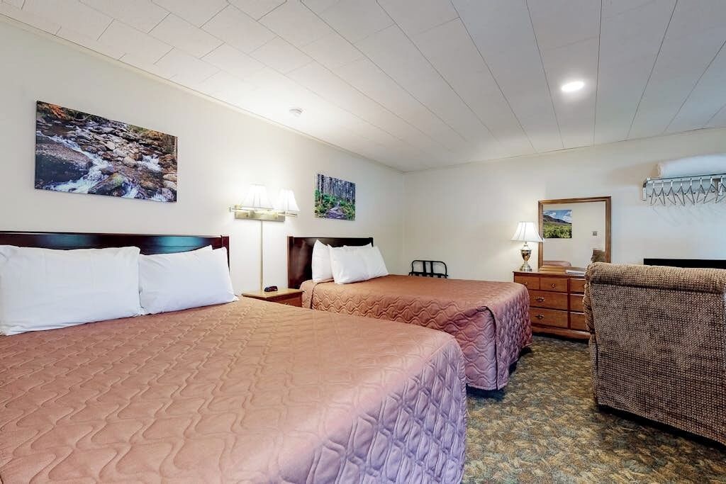A hotel room with two beds, a dresser, a chair, and wall art.
