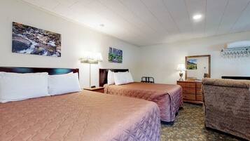 A hotel room with two beds, a dresser, a chair, and wall art.