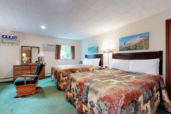Ein Hotelzimmer mit zwei Betten, einem Schminktisch, einem Sessel, einem Gemälde und einem Fenster.