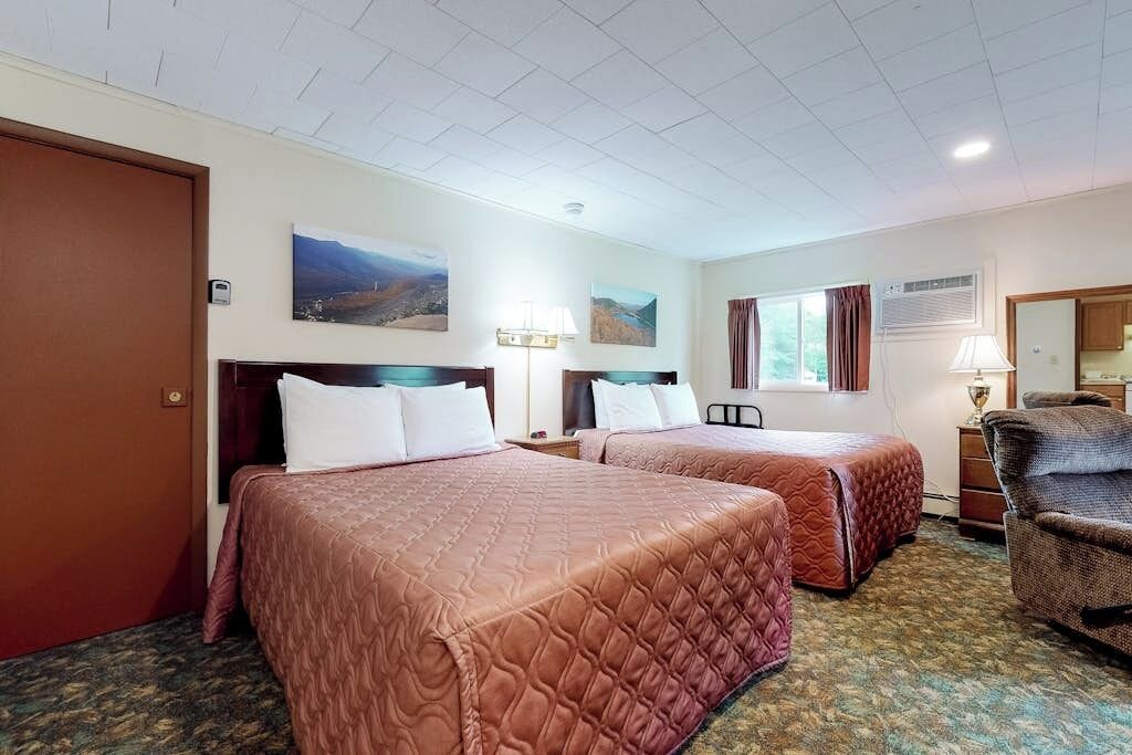 Een hotelkamer met twee bedden, een stoel, een bureau en een raam met gordijnen.