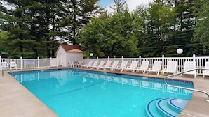 Une piscine rectangulaire entourée d’une clôture blanche et agrémentée de chaises longues.