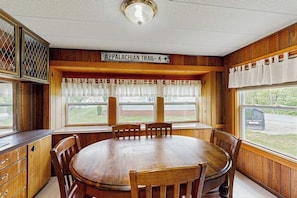 A wooden dining room with a table and chairs, a sign indicating the Appalachian Trail, and large windows with curtains.