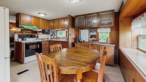 A kitchen with wooden cabinets, a dining table, and a view through a window.