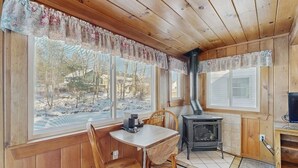 A wooden cabin interior with a table and chairs, a fireplace, and large windows with a view of a snowy landscape. - Eclectic Studio Cabin w/ Kitchenette, Free WiFi, Riverfront Location & More (Lincoln)