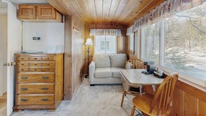 A cabin interior with a wooden ceiling, a sofa, a table, and a dresser. - Eclectic Studio Cabin w/ Kitchenette, Free WiFi, Riverfront Location & More (Lincoln)