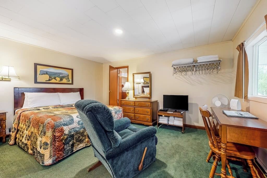 Een hotelkamer met een bed, een stoel, een bureau, een televisie, een dressoir en een raam met gordijnen.