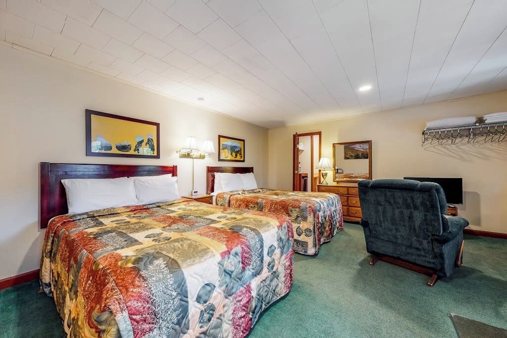 Een hotelkamer met twee bedden, een stoel, een televisie en kunstwerken aan de muren.