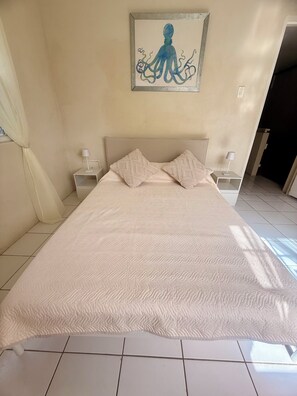 Une chambre à coucher avec un grand lit, deux tables de chevet, un tableau représentant une pieuvre et une porte donnant sur une autre pièce.
