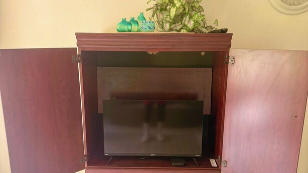 A wooden cabinet with a television on top, a small plant, and a wall clock. - Cozy 3-bedroom 2 and a half bathroom Townhome in beautiful Saint James with AC (Saint James)