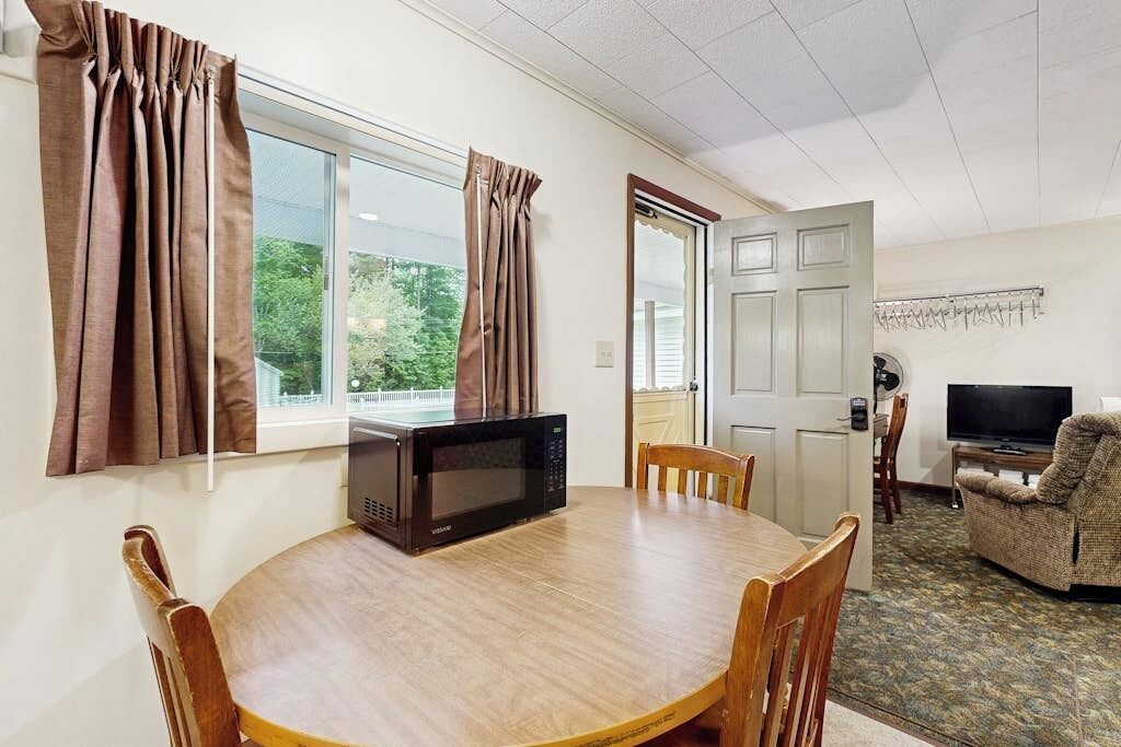 Ein Zimmer mit Esstisch, Stühlen, einer Mikrowelle, einem Fernseher und einer Tür.
