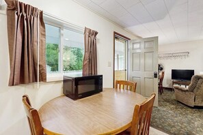 Une pièce comprenant une table à manger, des chaises, un four à micro-ondes, un téléviseur et une porte.