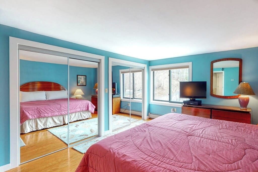 A bedroom with a bed, a television, a mirror, and a sliding door leading to another room.