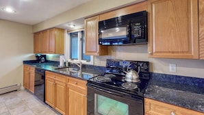 A kitchen with wooden cabinets, a black stove, a microwave, and a granite countertop.
