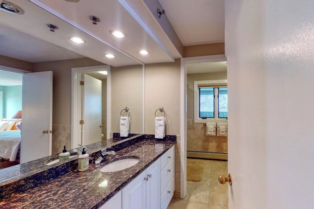 A modern bathroom with a granite countertop, a large mirror, and a shower area visible through an open door.
