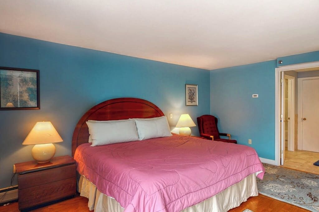 Un dormitorio con cama, dos lámparas de noche, una mesita de noche, una silla y una puerta.