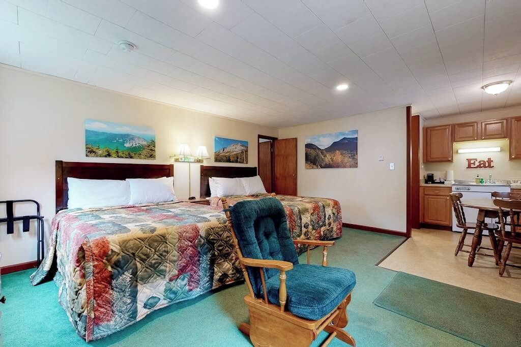 Een kamer met twee bedden, een schommelstoel, een kitchenette en kunstwerken aan de muur.