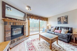 A living room with a fireplace, a sofa, a coffee table, and a large window with a view. - Comfy condo with spacious deck, fast WiFi, fireplace, indoor & outdoor pools (Lincoln)