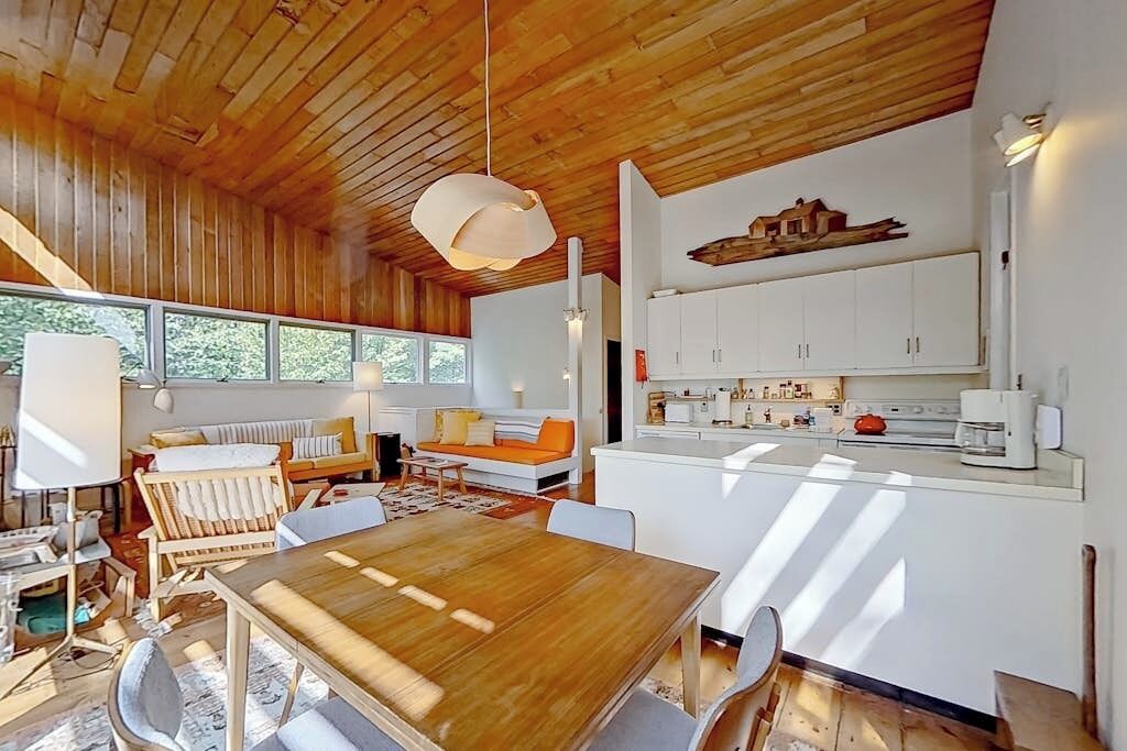 A modern interior with a wooden ceiling, a dining area with a wooden table, white cabinets, and a kitchen area.