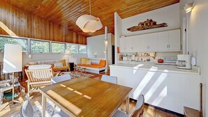 Un intérieur moderne avec un plafond en bois, un coin repas doté d’une table en bois, des meubles blancs et un espace cuisine.