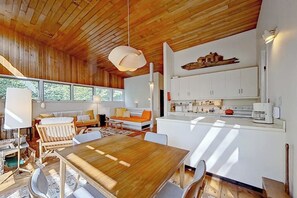 A modern interior with a wooden ceiling, a dining area with a wooden table, white cabinets, and a kitchen area.