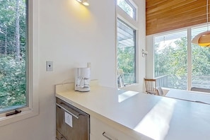 Una cocina moderna con cafetera, ventanas amplias y vistas a árboles.