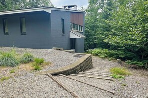 A modern building with a dark exterior, a sloped roof, and a gravel driveway leading to a wooden deck.