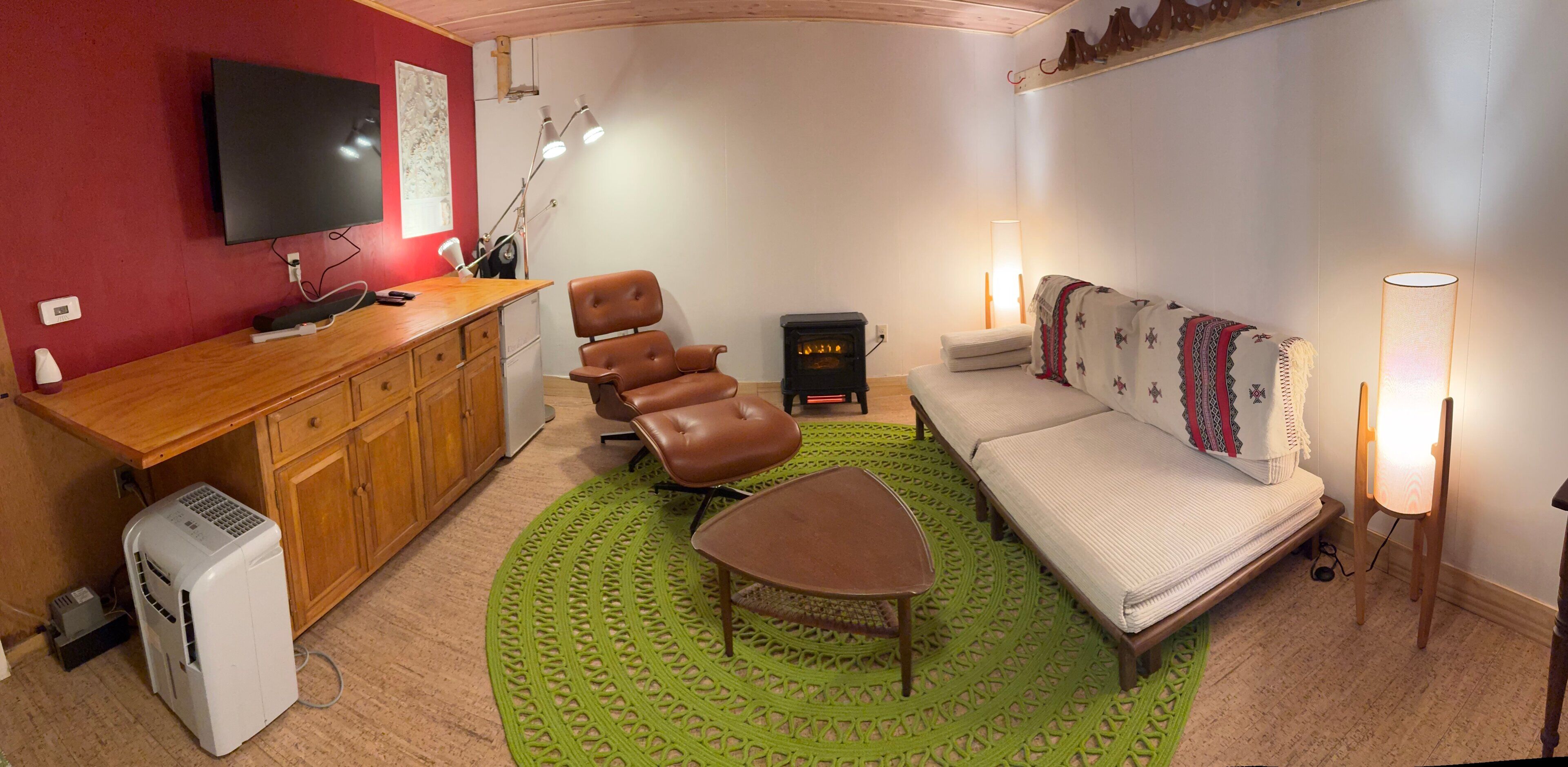 Un espace de vie compact comprenant un coin cuisine, un canapé, un fauteuil, une petite table, un radiateur et un téléviseur.