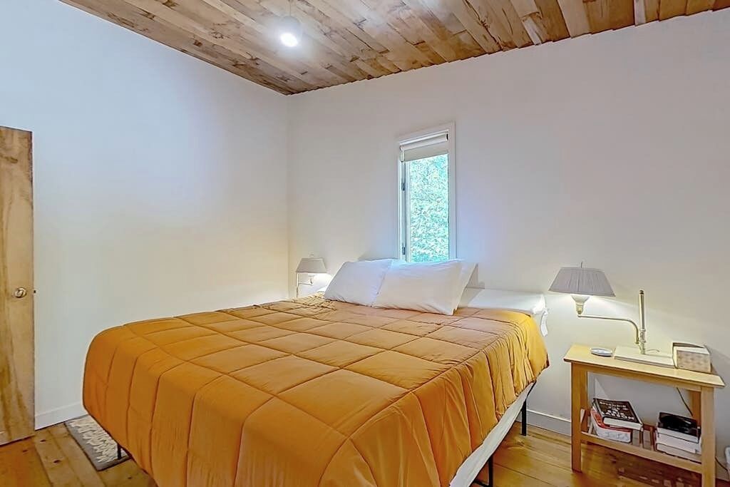 Un dormitorio con cama, ventana, mesita de noche y lámpara.