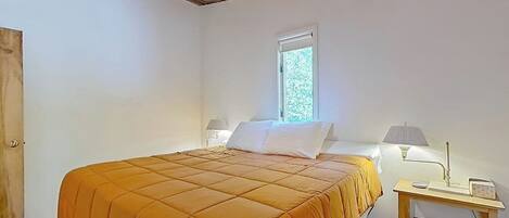 Un dormitorio con cama, ventana, mesita de noche y lámpara.
