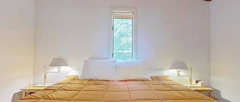 A bedroom with a bed, two bedside tables, lamps, a window, and a wooden ceiling.