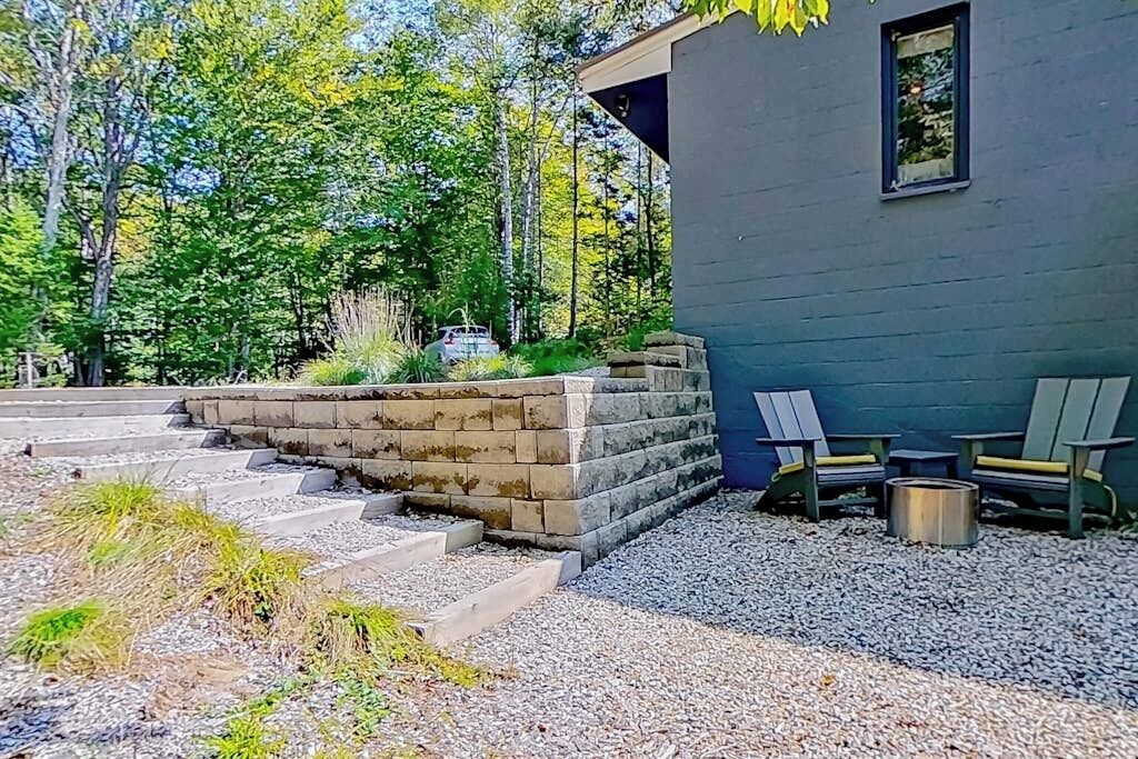 A modern building with a stone retaining wall, outdoor seating, and a gravel pathway.