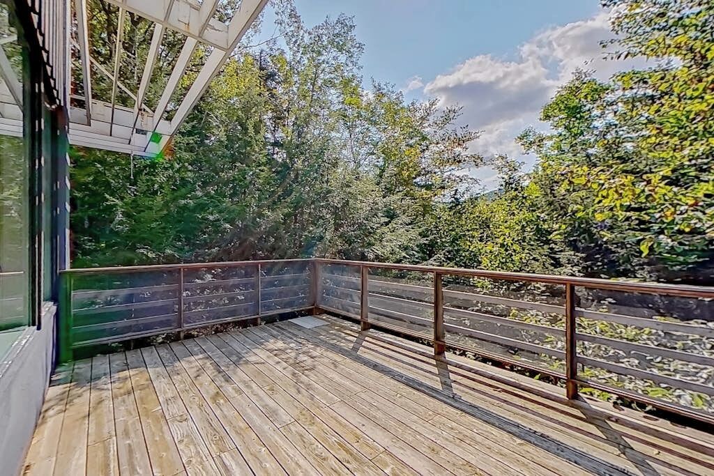 Une terrasse en bois avec des rampes en métal, entourée d’arbres et sous un ciel dégagé.