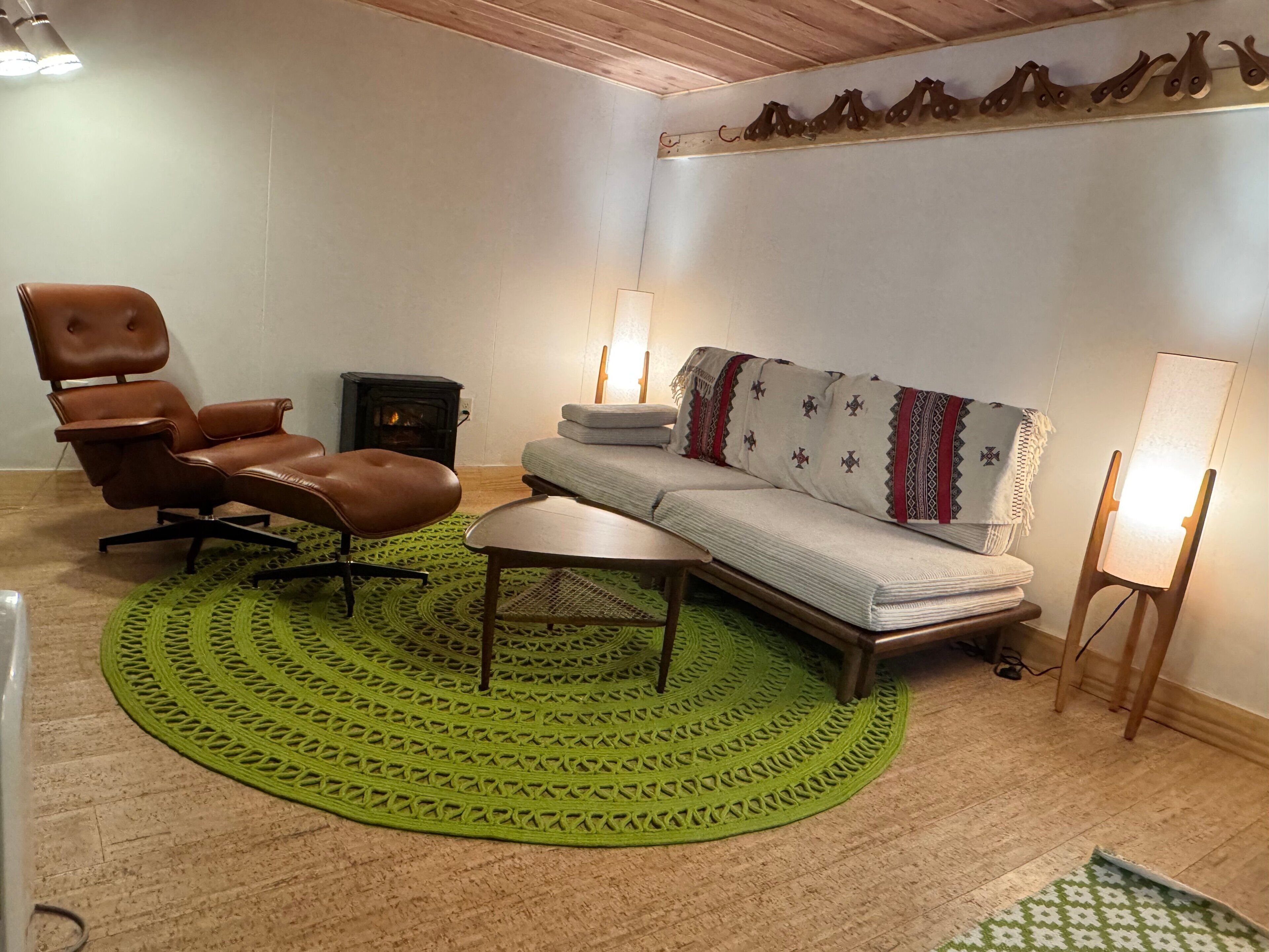 Ein gemütliches Wohnzimmer mit Ledersessel, einer Couch, einem kleinen Tisch und einem Teppich mit grünem Muster.