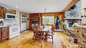 Un interno in legno con tavolo da pranzo, sedie, camino in pietra e una statua di un orso.