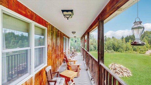 Un portico riparato con ringhiere in legno, diverse finestre e mobili da esterno.