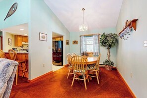A dining area with a round table and chairs, a chandelier, a potted plant, and a kitchen in the background. - Mountain-view, riverfront retreat with seasonal AC, pool, tennis, washer/dryer (Lincoln)