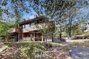 Ein modernes, zweistöckiges Haus mit Holzfassade, einer Veranda und einer natürlichen Umgebung mit Bäumen und einer Steinmauer.
