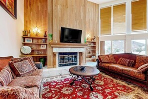 Ein Wohnzimmer mit Kamin, einer Couch, einem Fernseher und einem großen Fenster.