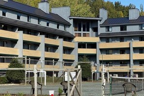Ein mehrstöckiges Gebäude mit Balkonen, einer überdachten Außenbestuhlung und einem Volleyballnetz.