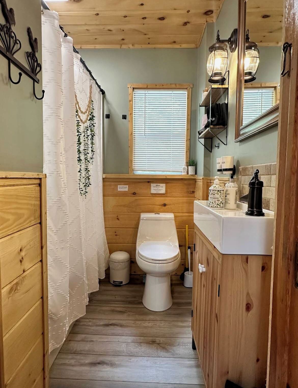 Een houten badkamer met een badkamerkastje, toilet en douchegordijn.