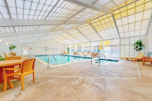 Ein Innenpool mit hoher Decke, der durch große Fenster hell erleuchtet wird, mit Liegestühlen rund um das Becken.