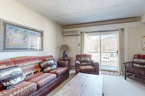 Ein Wohnzimmer mit einer Couch, einem Sessel und einem Couchtisch, einer Karte an der Wand und einer Glastür zum Balkon.