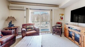 Un soggiorno con divano, poltrona, tavolino, televisione e una porta scorrevole in vetro che dà su un balcone.