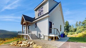 Ein modernes, zweistöckiges Haus mit einer Veranda und einer Treppe, die zu der oberen Etage führt, mit Blick auf die umliegende Landschaft.