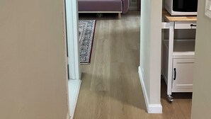 Ein Flur, der in einen Wohnbereich mit einer Couch, einer Mikrowelle und einem Schrank führt.